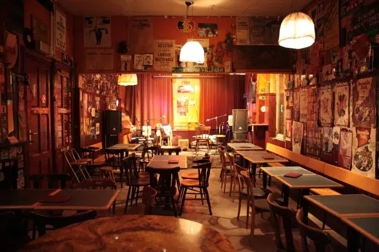 Het interieur van Toogenblik: houten tafels, rode gordijnen en affiches aan de muur
